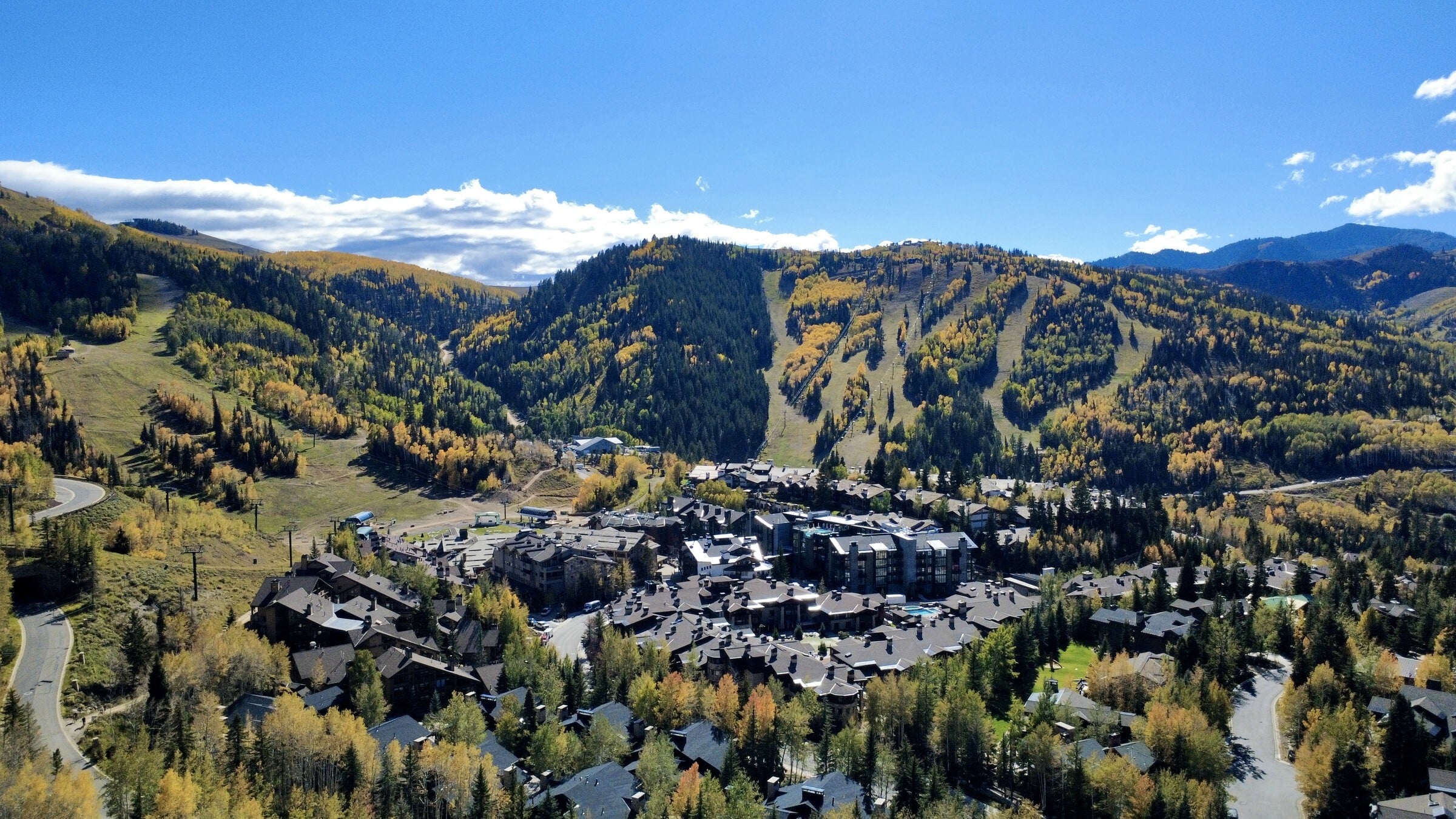 Aerial view of a Park City mountain village in fall, with ski runs and gold aspens under a clear blue sky.